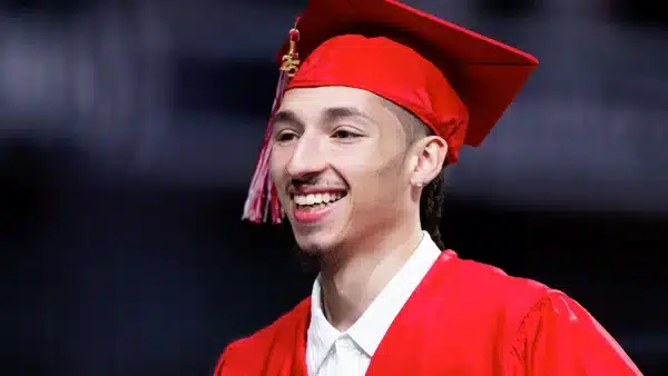 Man graduating in red cap and gown.